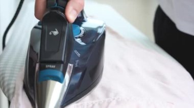 Ütü masasında açık pembe pantolon ütüleyen bir kadın. Elektrikli ütü tutan kadın, ev işleri. Rutin ev işleri. Yüksek kalite 4k görüntü