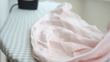 Su püskürten ve ütü masasında açık pembe pantolon giyen bir kadın. Demirden sıcak kökler. Elektrikli ütü tutan kadın, ev işleri. Rutin ev işleri. Yüksek kalite 4k görüntü