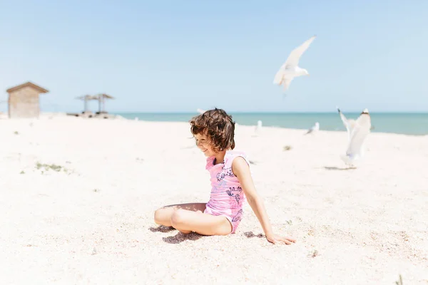 stock image happy child girl wearing swimsuit sitting on beach in the day time. Lifestyle photography. Pastel colors