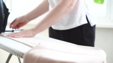 Ütü masasında açık pembe kapüşonlu kadın ütülüyor. Demirden sıcak kökler. Elektrikli ütü tutan kadın, ev işleri. Rutin ev işleri. Yüksek kalite 4k görüntü
