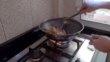 Fırında yemek ve güçlü bir ateşle tava. Tavada yemek pişiren bir kadın vardı..