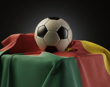 Düzenli bir futbol topu, izole edilmiş bir stüdyo arka planında bir kaideye sarılı bir Kamerun bayrağı üzerinde dinleniyor.