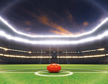 A red aussie rules ball on the center line of a stadium with posts on a marked green grass pitch at night under illuminated floodlights - 3D render clipart