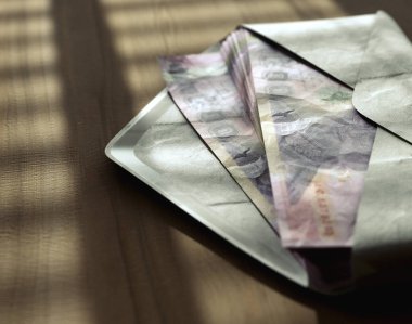 Huysuz ışıklandırmanın altında ahşap bir yüzey üzerinde bir zarfın içinde yayılan banknotlar yığını.