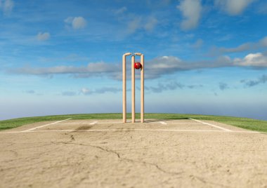 Kırmızı bir kriket topu ahşap kriket kalelerine çarpıyor ve gökyüzü arka planında kefaletler çıkıyor.