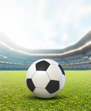 Gündüz vakti yeşil çimlerin üzerinde futbol topunu mavi bulutlu bir gökyüzünün altında gösteren sıradan bir futbol stadyumu.