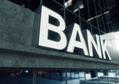 Gece vakti açıkta duran beton ve yansıtıcı camlardan yapılmış modern bir banka binasının girişinin üstündeki işaret.