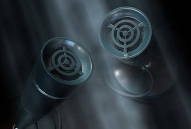 Karanlık bir arka planda, sisli bir spot ışığı altında iki adet eski masa mikrofonunun üç boyutlu canlandırması, podcast markalaşma, yayın ve retro ses pazarlama projeleri için mükemmel..