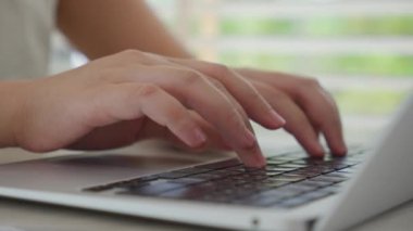 Genç bir iş kadınının eli bilgisayarda klavyede çalışmakla meşgul. Ev ofis masasında oturup internette çalışıyor.