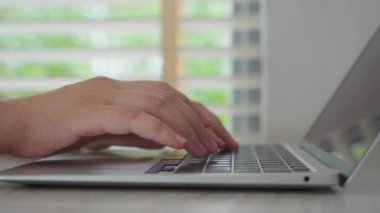 Genç bir iş kadınının eli bilgisayarda klavyede çalışmakla meşgul. Ev ofis masasında oturup internette çalışıyor.