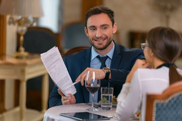 Businessman talking with woman and showing documents in hotel restaurant. High quality photo