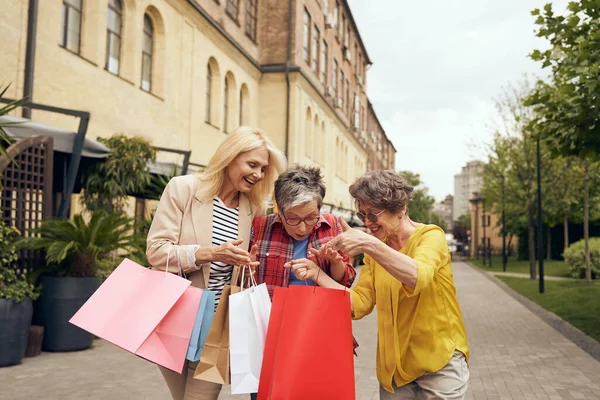 Joyful old women friends after shopping having fun while walking outdoors. Seasonal sales