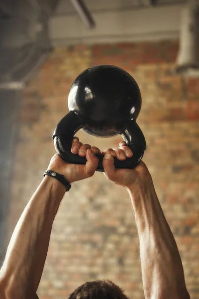 Cropped photo of strong man hands holding big dumbbell under his head while exercising at gym. Weight exercises
