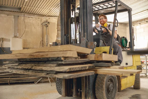 Male craftsman at wooden sawmill warehouse is loading with loader wooden board. High quality photo