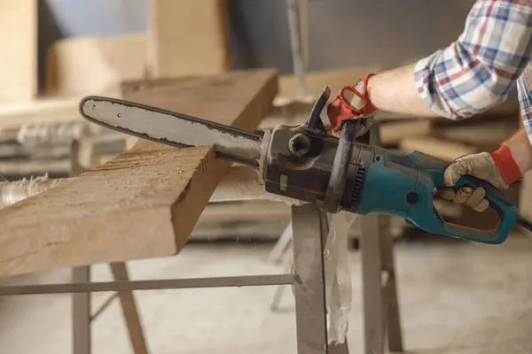 Close up of woodworker is cutting wood with chainsaw on carpentry workshop. High quality photo