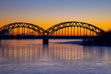 Letonya 'nın başkenti Riga' daki donmuş Daugava nehri üzerinde demir köprüsü olan güzel bir gündoğumu manzarası. Kuzey Avrupa 'nın kış manzarası.