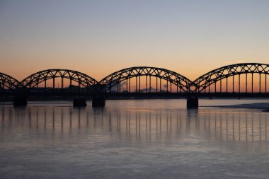 Letonya 'nın başkenti Riga' daki donmuş Daugava nehri üzerinde demir köprüsü olan güzel bir gündoğumu manzarası. Kuzey Avrupa 'nın kış manzarası.