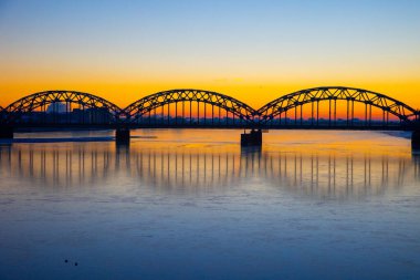 Letonya 'nın başkenti Riga' daki donmuş Daugava nehri üzerinde demir köprüsü olan güzel bir gündoğumu manzarası. Kuzey Avrupa 'nın kış manzarası.