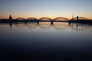 Letonya 'nın başkenti Riga' daki donmuş Daugava nehri üzerinde demir köprüsü olan güzel bir gündoğumu manzarası. Kuzey Avrupa 'nın kış manzarası.