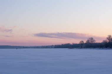 Donmuş göl ve ormanın güzel bir kış gündoğumu manzarası. Kuzey Avrupa 'da şafak vakti gökyüzü ile renkli manzara.