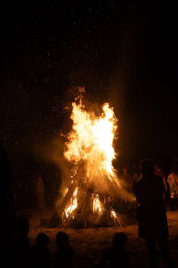 İnsanlar yaz aylarında Ateş Festivali sırasında Baltık Denizi sahilinde ateşin yanmasını izliyor. Parlak, sıcak ateş.