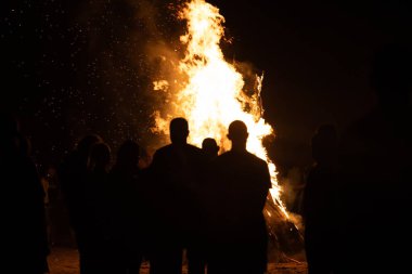 İnsanlar yaz aylarında Ateş Festivali sırasında Baltık Denizi sahilinde ateşin yanmasını izliyor. Parlak, sıcak ateş.