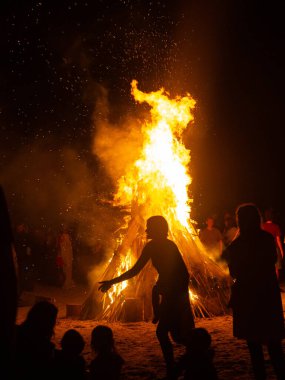 İnsanlar yaz aylarında Ateş Festivali sırasında Baltık Denizi sahilinde ateşin yanmasını izliyor. Parlak, sıcak ateş.
