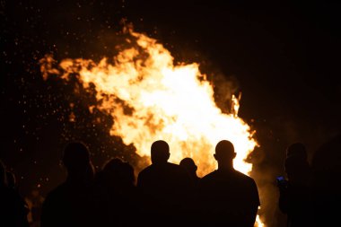 İnsanlar yaz aylarında Ateş Festivali sırasında Baltık Denizi sahilinde ateşin yanmasını izliyor. Parlak, sıcak ateş.
