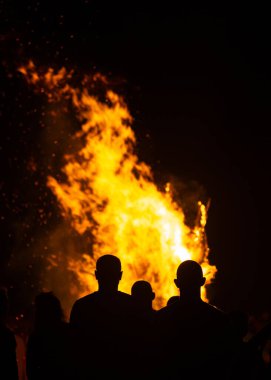 İnsanlar yaz aylarında Ateş Festivali sırasında Baltık Denizi sahilinde ateşin yanmasını izliyor. Parlak, sıcak ateş.