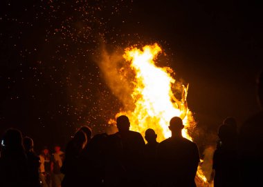 İnsanlar yaz aylarında Ateş Festivali sırasında Baltık Denizi sahilinde ateşin yanmasını izliyor. Parlak, sıcak ateş.