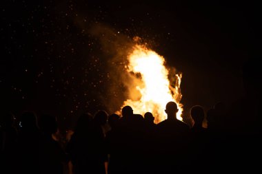 İnsanlar yaz aylarında Ateş Festivali sırasında Baltık Denizi sahilinde ateşin yanmasını izliyor. Parlak, sıcak ateş.