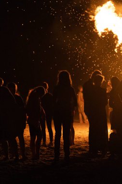 İnsanlar yaz aylarında Ateş Festivali sırasında Baltık Denizi sahilinde ateşin yanmasını izliyor. Parlak, sıcak ateş.