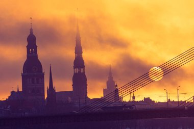 A beautiful Riga cityscape with suspension bridge over the riwer during colorful sunrise. Buildings against colorful sky. Norther Europe morning with warm sky.