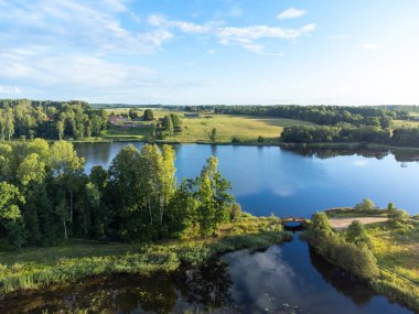 Yeşil yaz ağaçları ve tarlalar arasında küçük bir göl manzarası. Letonya, Kuzey Avrupa 'da kırsal alanların doğal manzarası.