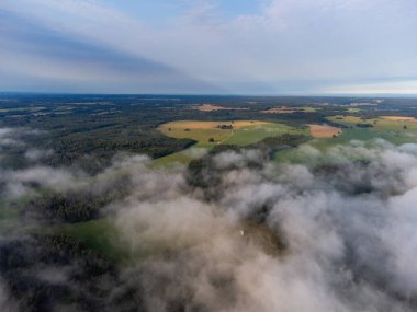 Letonya kırsalının yaz manzarasını kaplayan yumuşak beyaz sis. Sis bulutlarının hava fotoğrafçılığı.