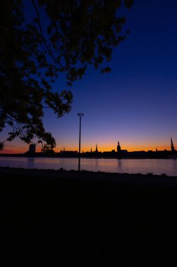 Riga, Letonya 'nın yaz gündoğumunda güzel bir şehir merkezi panoraması. Parlak gökyüzüne karşı siluetler inşa eden renkli bir manzara.