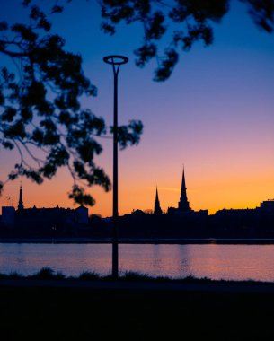 Riga, Letonya 'nın yaz gündoğumunda güzel bir şehir merkezi panoraması. Parlak gökyüzüne karşı siluetler inşa eden renkli bir manzara.