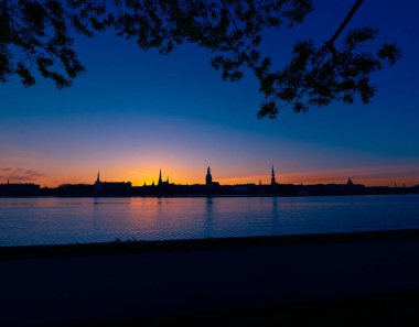 Riga, Letonya 'nın yaz gündoğumunda güzel bir şehir merkezi panoraması. Parlak gökyüzüne karşı siluetler inşa eden renkli bir manzara.