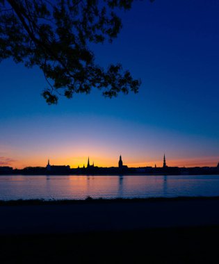 Riga, Letonya 'nın yaz gündoğumunda güzel bir şehir merkezi panoraması. Parlak gökyüzüne karşı siluetler inşa eden renkli bir manzara.