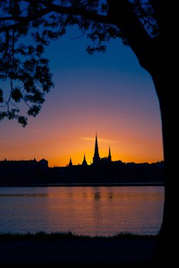 Riga, Letonya 'nın yaz gündoğumunda güzel bir şehir merkezi panoraması. Parlak gökyüzüne karşı siluetler inşa eden renkli bir manzara.