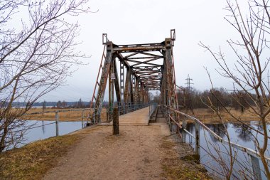 Bulutlu bahar gününde nehrin üzerindeki metal bir köprü. Riga, Letonya 'da doğal ilkbahar manzarası.