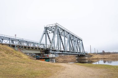Bulutlu bahar gününde nehrin üzerindeki metal bir köprü. Riga, Letonya 'da doğal ilkbahar manzarası.