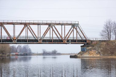 Bulutlu bahar gününde nehrin üzerindeki metal bir köprü. Riga, Letonya 'da doğal ilkbahar manzarası.