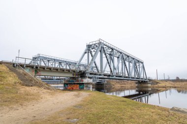 Bulutlu bahar gününde nehrin üzerindeki metal bir köprü. Riga, Letonya 'da doğal ilkbahar manzarası.