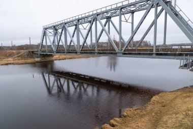Bulutlu bahar gününde nehrin üzerindeki metal bir köprü. Riga, Letonya 'da doğal ilkbahar manzarası.