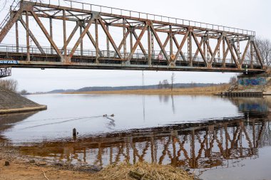 Bulutlu bahar gününde nehrin üzerindeki metal bir köprü. Riga, Letonya 'da doğal ilkbahar manzarası.