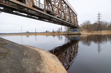 Bulutlu bahar gününde nehrin üzerindeki metal bir köprü. Riga, Letonya 'da doğal ilkbahar manzarası.