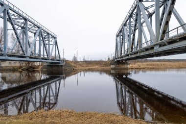 Nehir üzerinde demiryolu rayları olan iki paralel metal köprü. Riga, Letonya 'nın ilkbahar manzarası.