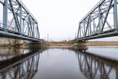 Nehir üzerinde demiryolu rayları olan iki paralel metal köprü. Riga, Letonya 'nın ilkbahar manzarası.