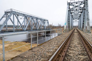 Nehir üzerinde demiryolu rayları olan iki paralel metal köprü. Riga, Letonya 'nın ilkbahar manzarası.